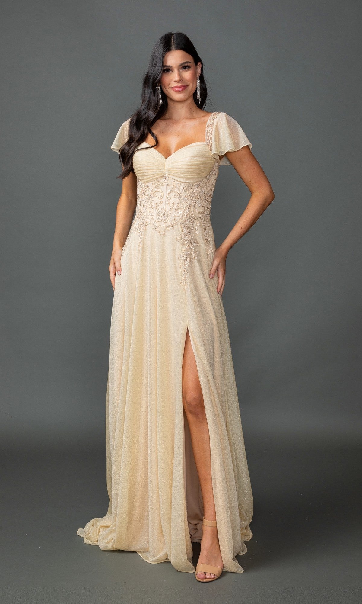 A woman poses against a gray background in the Dancing Queen 4496 short-sleeve long formal dress in champagne, featuring glitter lace, flutter sleeves, a sweetheart neckline, and a thigh-high slit.